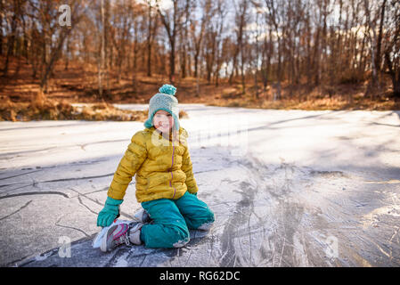 Retrato de un sonriente vestida de patines de hielo sentado en un estanque congelado, Estados Unidos