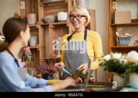 Cintura para arriba retrato del dueño de la tienda de flor madura hablando al empleado y sonriente, espacio de copia