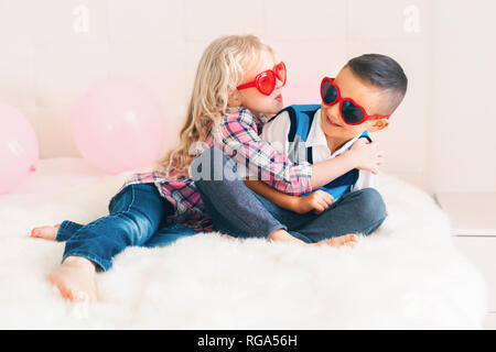Retrato de dos feliz caucásicos blancos adorable lindo gracioso niños portando gafas con forma de corazón. Chica tratando de besar a un chico. El amor, la amistad y la diversión. V Foto de stock