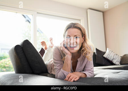 Retrato de mujer de risa tumbado en sofá en casa Foto de stock
