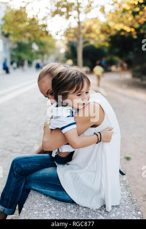 Madre sentada en un banco, abrazando con su hijo Foto de stock