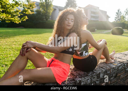 Retrato de hermanas gemelas sentados espalda con espalda en una pared en verano relajante