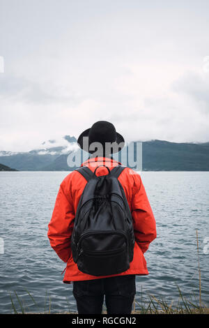 Joven parado por el agua, mirando a la distancia, vista trasera