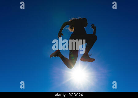 Sportive joven saltando bajo un cielo azul con luz de fondo Foto de stock