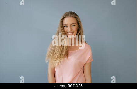 Retrato de mujer sonriente vistiendo camiseta rosada delante de fondo gris Foto de stock