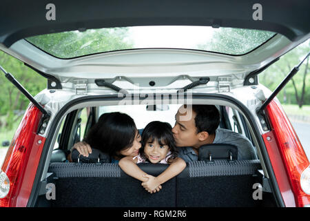 Feliz niña en un coche porque la madre y el padre amándola con besos