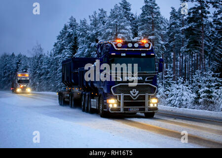 Salo, Finlandia - 25 de enero de 2019: dos camiones Scania V8 para el acarreo de piedra caliza en la parte delantera en velocidad con bonitas luces iluminando el oscuro camino rural Foto de stock