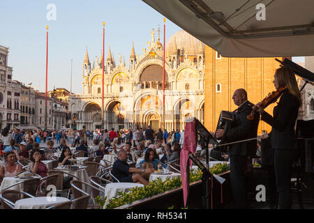 Los turistas disfrutar de bebidas en el café Florian, en Piazza San Marco, con música en vivo de la banda en frente de la Catedral de San Marcos al atardecer Foto de stock