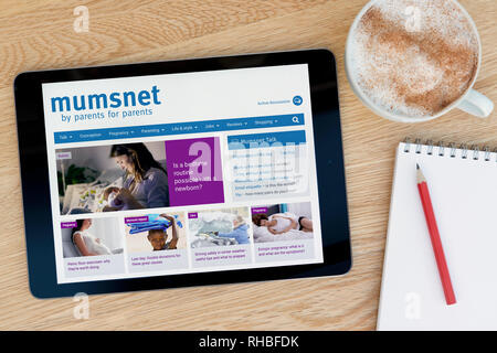 Las características del sitio web Mumsnet en un dispositivo tablet iPad que descansa sobre una mesa de madera junto a un bloc de notas (sólo para uso editorial). Foto de stock