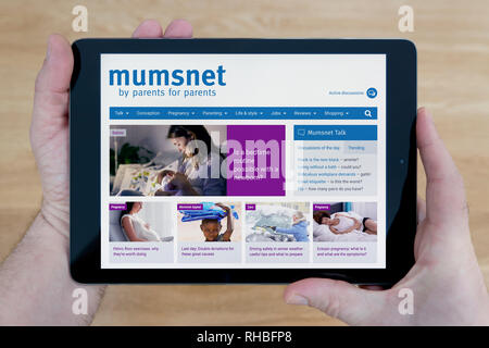 Un hombre se ve en el sitio web de Mumsnet en su iPad dispositivo tablet, disparó contra una mesa de madera de fondo (sólo para uso editorial). Foto de stock