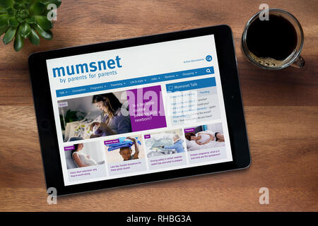 El sitio web de Mumsnet es visto en un iPad, en una mesa de madera junto con un café espresso y una planta de casa (Editorial). Foto de stock
