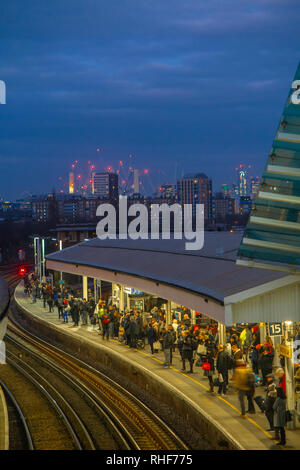 Los trenes en Clapham Junction Station al anochecer con el Battersea Power Station en el fondo y de pasajeros en la plataforma Foto de stock