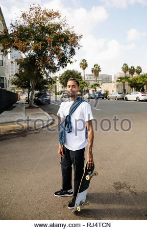 Retrato seguros, cool Latinx joven con el monopatín en la calle urbana