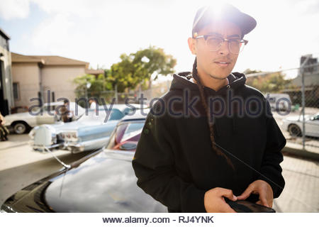 Seguro Latinx retrato joven con trenza larga apoyada sobre coches antiguos en un soleado día de estacionamiento