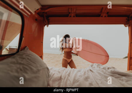 Mujer joven surfista quitar tablas de surf en la playa de vehículos recreativos, Jalama, California, EE.UU.
