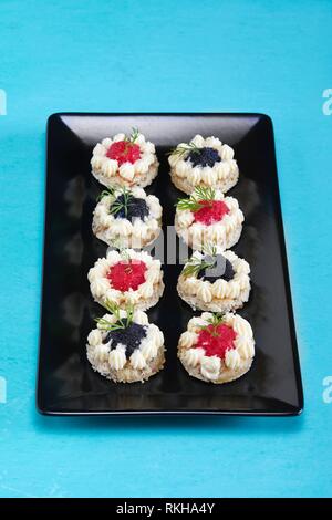 Placa con canapés de caviar rojo y negro adornado con eneldo.