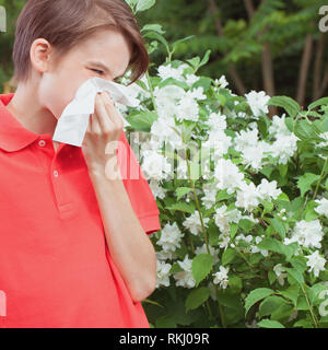 Adolescente varón con la gripe estacional sonarse la nariz en un tejido en spring garden - Concepto de infección estacional Foto de stock