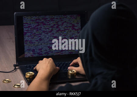 Peligroso hacker encapuchados en portátil rompe la seguridad informática sistem y robar cryptocurrency bitcoin Foto de stock