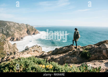 Un turista con una mochila en la cima de un acantilado admira una hermosa vista del océano Atlántico en Portugal. Foto de stock