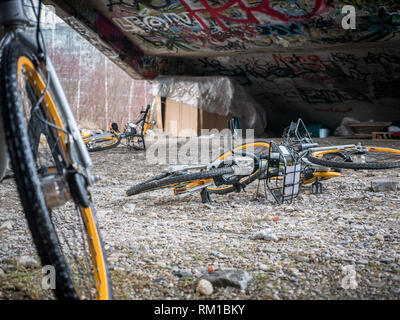 Vieja chatarra amarillo bicicletas bajo escaleras de cemento con graffiti y sin hogar refugio para dormir Foto de stock