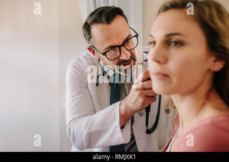 ENT médico en busca del paciente femenina en el oído con un instrumento. Examen médico varón del oído del paciente con el otoscopio en su clínica. Foto de stock