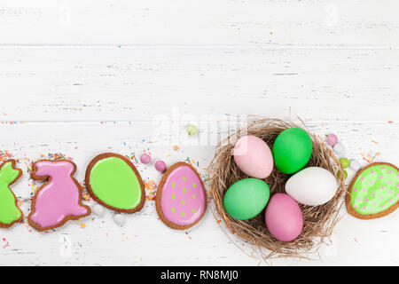 Tarjeta de felicitación de Pascua con coloridas galletas de jengibre y los huevos de pascua en el nido. Vista superior de la tabla de madera con espacio para sus saludos Foto de stock