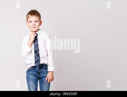 Un pequeño chico de moda posando frente a una pared de concreto gris-azul.  Retrato de un niño sonriente vestido con un suéter y un bro de rayas negras  y amarillas Fotografía de