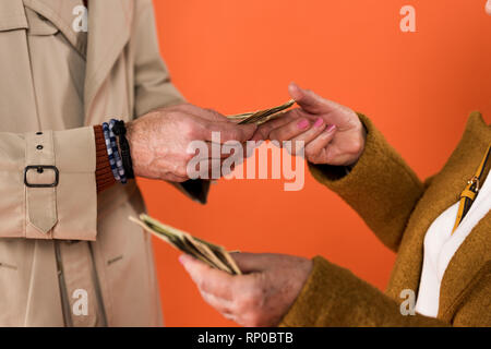 Vista recortada de alto par la celebración de billetes de dólar en manos aisladas sobre naranja