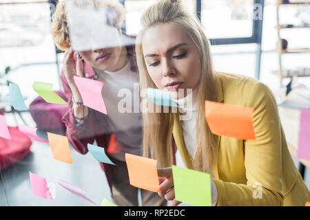 Empresario casual y empresaria poniendo colorido notas rápidas sobre el cristal de ventana en la oficina Foto de stock