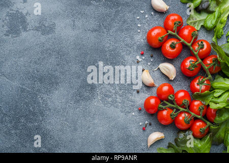 Tomates Cherry en una sucursal de hierbas frescas y el diente de ajo con especias sobre una mesa de piedra oscura vista superior con espacio de copia