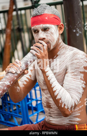 Un músico callejero tocando un digeridoo en Sydney Australia pintadas en blanco cuerpo forman aborigen Foto de stock