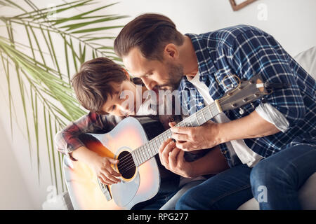 Padre e hijo pequeño en casa sentados en el sofá chico con guitarra papá  mostrando los acordes reflexivos Fotografía de stock - Alamy