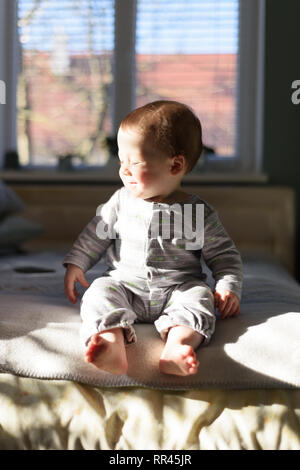 Happy Baby Boy en gris pijama sobre la cama en su habitación