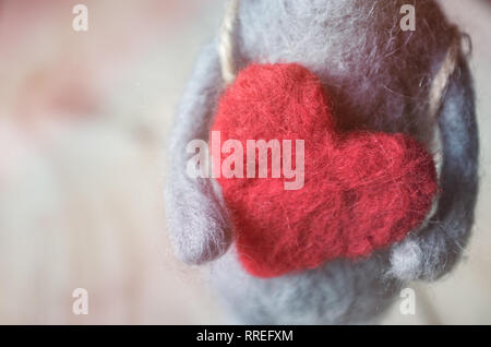 Ratón de juguete de lana en manos de un gran corazón rojo Foto de stock