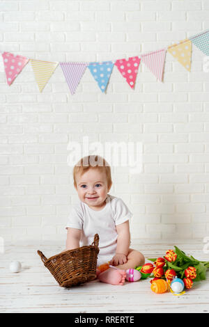 Niño lindo muchacho sentado con los huevos de Pascua y tulipanes contra el fondo blanco. Foto de stock