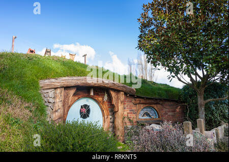 Hobbiton movie set, Matamata, en Nueva Zelanda. . Pintoresco pequeño Hobbit casa con puerta azul, en un verde paisaje de colinas y cielo azul