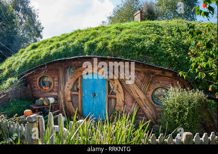 Hobbiton movie set, Matamata, en Nueva Zelanda. . Pintoresco pequeño Hobbit casa con puerta de color turquesa, en un paisaje de colinas verdes, sol y cielo azul