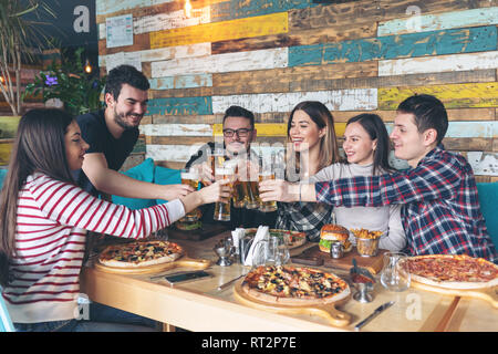 Feliz jóvenes amigos brindando con cerveza en el partido en el pub de moda