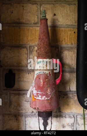 Un vintage rojo extintor colgado en una pared con una etiqueta y desapareció en forma de cono Foto de stock