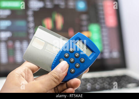 Mano sujetando el teléfono e internet security key y tarjeta de ATM con el monitor que muestra como fondo de transacción por internet Foto de stock