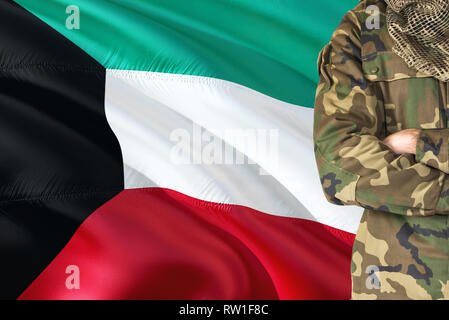 Soldado Kuwaití de brazos cruzados con las banderas ondeantes sobre fondo - Kuwait tema militar. Foto de stock
