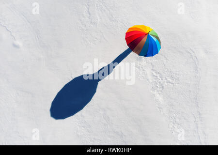 Alguien bajo el paraguas de arco iris de colores en campo blanco de nieve. Vista superior