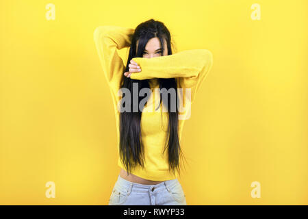 Vestida con un suéter amarillo cubre su cara en un fondo amarillo Foto de stock