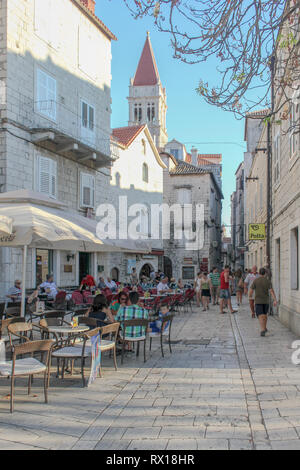 Los turistas relajarse temprano en una noche de verano en la cafetería y bares a lo largo de uno de Trogir las antiguas callejuelas. Foto de stock