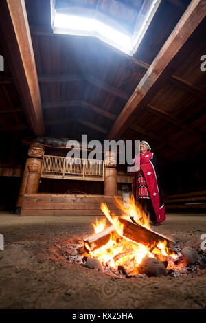 Una de las primeras naciones vestida de elder regalia tradicional está al lado de un fuego en el bighouse en la aldea de Oweekeno. Wuikinuxv, Ríos Inlet, Br Foto de stock