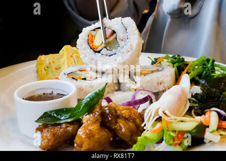 Plato lleno de plato asiático la comida con los palillos, recogiendo el sushi laminados