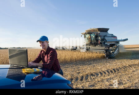Una granja niña usa un ordenador portátil como un campo de trabajo de la cosechadora durante la cosecha de soja, cerca de Lorette, Manitoba Foto de stock