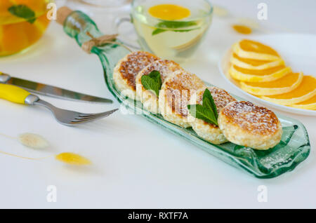 Buñuelos de queso cottage con moras, menta y crema agria para desayuno saludable en un plato para servir transparente.tetera con té de desintoxicación. Dieta des Foto de stock