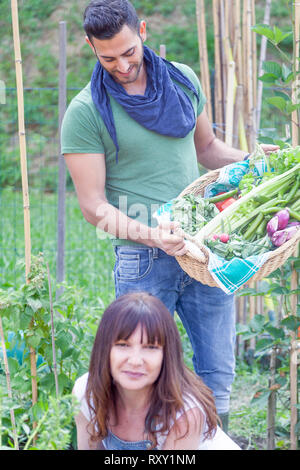 Pareja joven de jardineros recopila las hortalizas frescas en gardenhouse Foto de stock