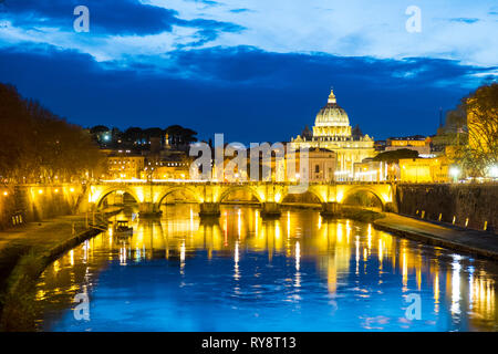 Bellamente iluminado con vista al río de el Ponte Sant'Angelo y la Ciudad del Vaticano la Basílica de San Pedro al anochecer, en Roma, Italia, durante el invierno Foto de stock